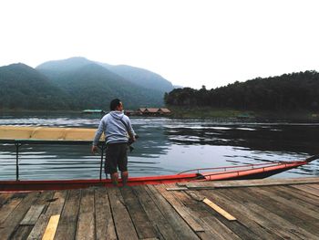 Rear view of man on boat on lake against sky