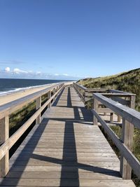 View of wooden walkway leading towards sea against clear sky