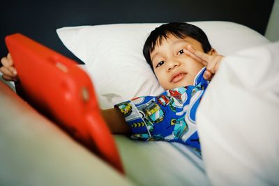 Portrait of cute boy gesturing while lying on bed at home