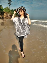 Full length of woman in sunglasses and sun hat standing at beach