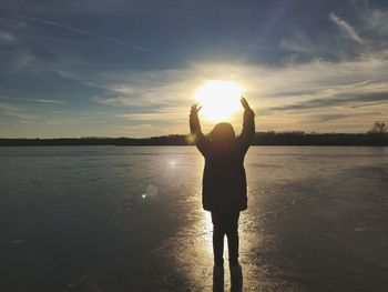 Rear view of man standing in water at sunset