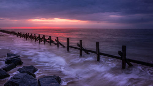 Wooden posts in sea against sky during sunset