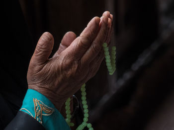 Cropped hand of woman with necklace praying in darkroom