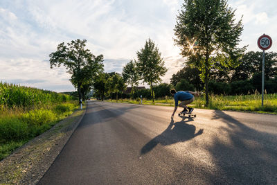 Rear view of man skateboarding on road sunny day