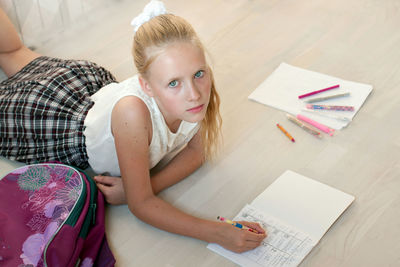 Portrait of girl doing homework while lying down on hardwood floor