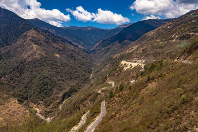 Mountain valley with curvy road and bright blue sky at sunny day from top