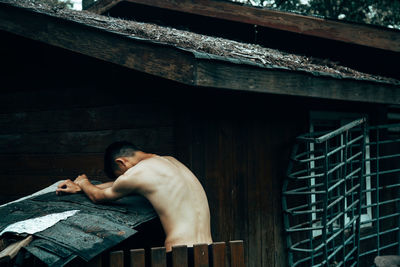 Shirtless man by wooden house