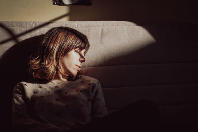 Young woman looking down while sitting on wall at home