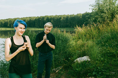 Friends smoking electronic cigarette at lakeshore