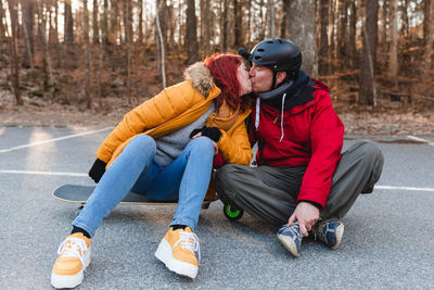 Delighted couple sitting on skateboard and scooter while kissing and having fun on parking in autumn