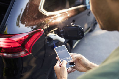 Man using mobile phone while standing by charging electric car