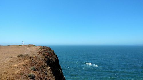 Scenic view of cliff by sea against clear blue sky