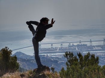 Woman exercising on cliff against sea