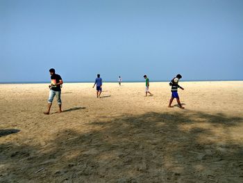 People walking on beach against clear sky