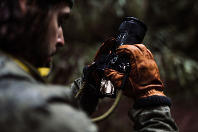 Unrecognizable male traveler taking photo on professional photo camera while standing in woods in fall