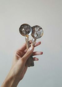 Cropped hand holding spoons against white background