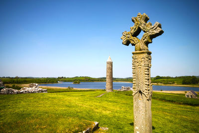 Irish round tower and celtic cross against blue sky at county fermanagh