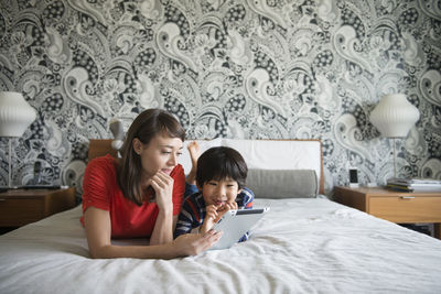 Mother and son using digital tablet while lying on bed