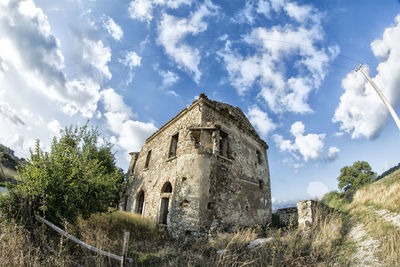 Low angle view of abandoned building against cloudy sky