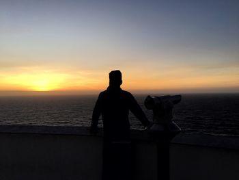 Silhouette man sitting at beach against sky during sunset