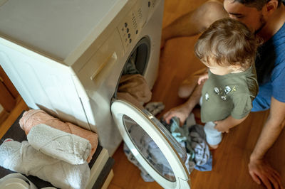 Son with father loading clothes in washing machine