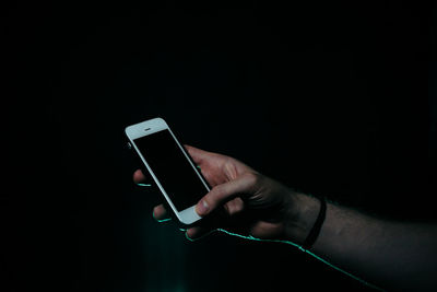 Close-up of hand holding mobile phone against black background