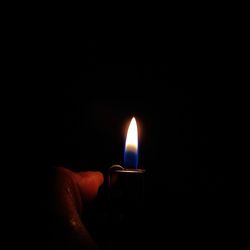 Close-up of hand holding lit candle in darkroom