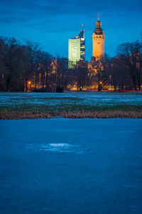 Illuminated building by lake against blue sky