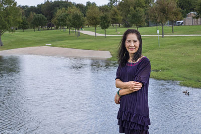 Portrait of smiling woman standing against lake in park
