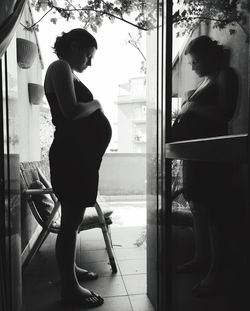 Side view of woman sitting on window at home