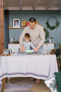 Dad and little son roll out the dough in the kitchen for christmas ginger cookies or gingerbread