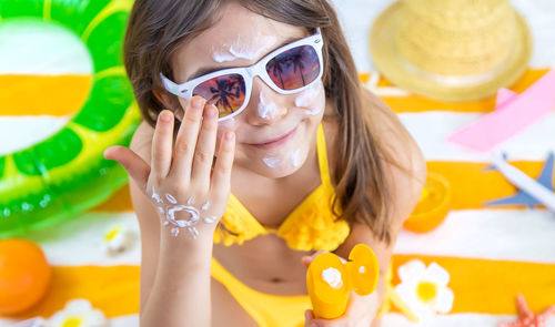 Happy girl wearing sunglasses applying suntan lotion