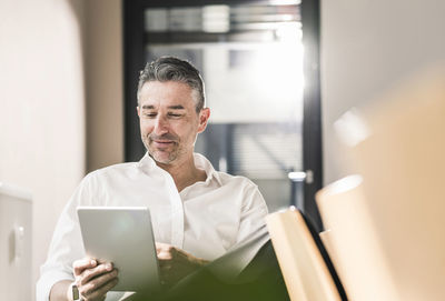 Content businessman sitting in his office using tablet