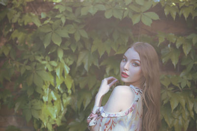 Portrait of beautiful young woman standing by plants in park