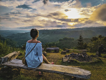 Rear view of teenage girl sitting on seat during sunset
