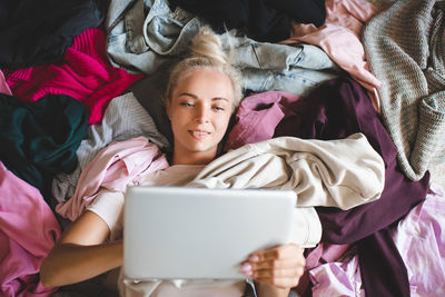 Young pretty woman lying on floor in pile of different clothes purchase new clothes on internet