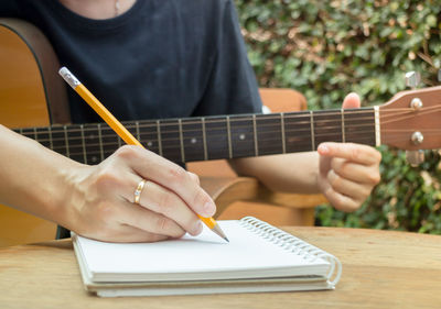 Midsection of men writing on diary while playing guitar