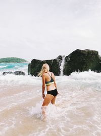 Rear view of woman standing by rock at beach against sky