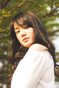 Close-up portrait of young woman standing against trees