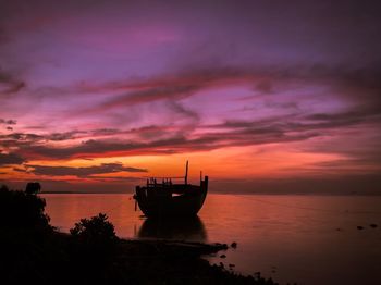 Boat moored in sea against dramatic sky during sunset