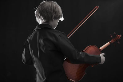 Boy playing violin against black background