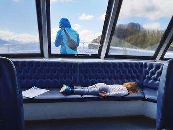 Full length of girl sleeping on seat while mother standing on deck against sky