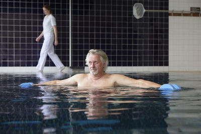 Water surface level view of shirtless mature man with dumbbells in swimming pool