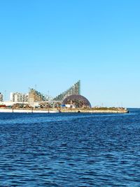 Scenic view of sea by buildings against clear blue sky