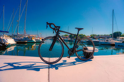 Road bike in front of sailboats moored in harbor against clear blue sky