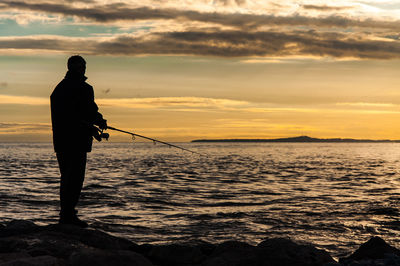 Silhouette of person holding sea against sky during sunset