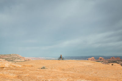 Woman sits on mountain bike on mountain rock plateau in moab utah american southwest. 