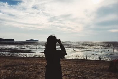 Silhouette woman photographing at beach against sky