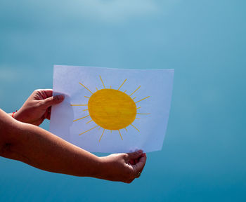 Midsection of woman holding paper against blue sky