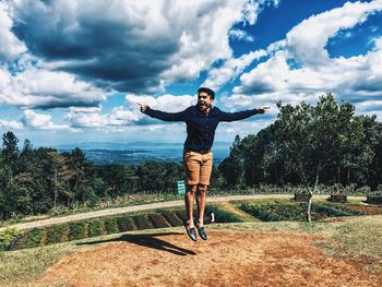 Young man jumping on field against cloudy sky